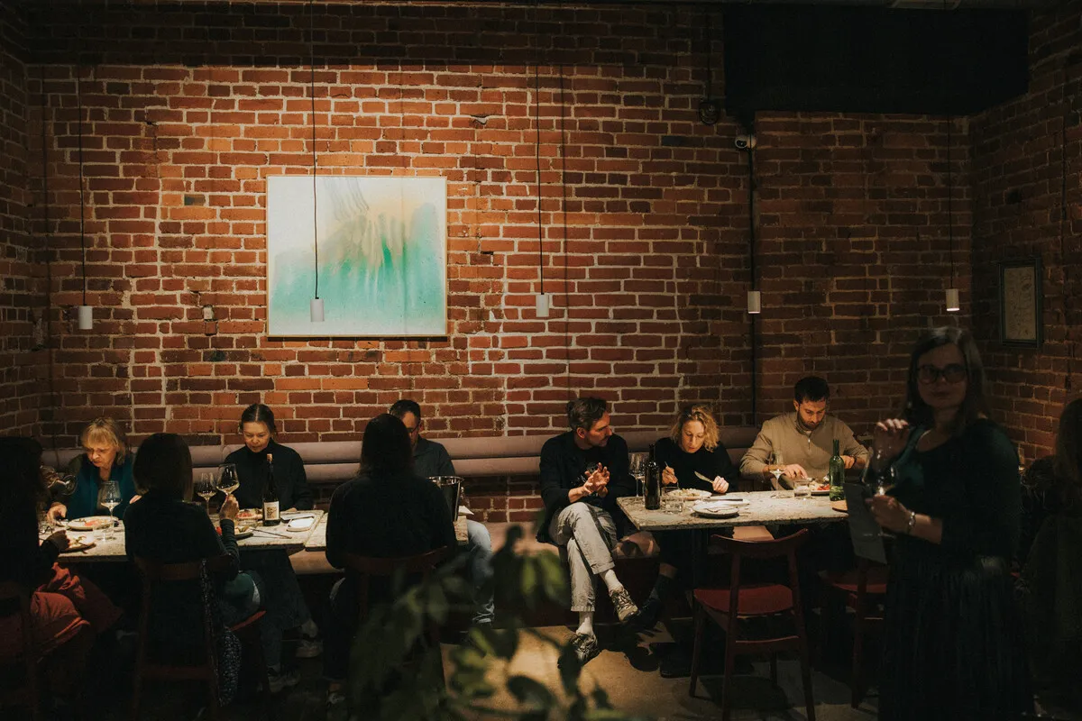 Degustacja wina w Pijalnych — goście przy stole, ceglane ściany, ciepłe światło