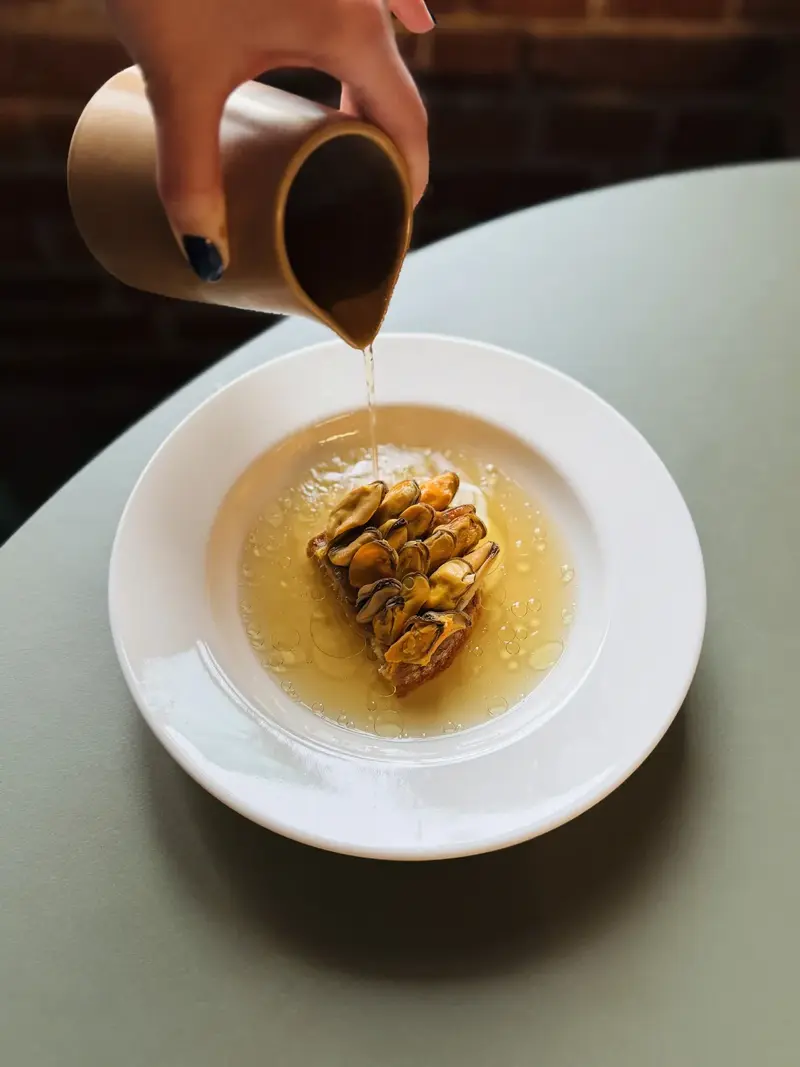Sauce being poured over a grilled dish — Tomek Wencek's fire-based cooking at Pijalni