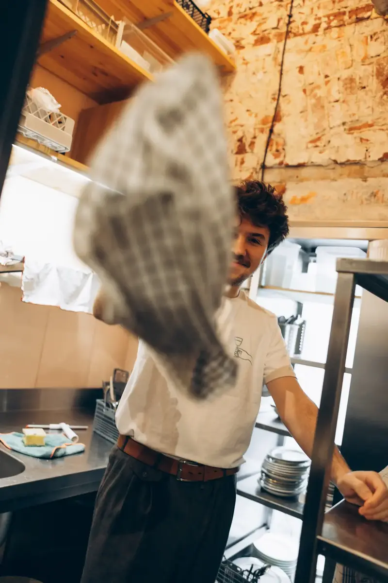 Tomek Wencek working the grill at Pijalni — smoke rising from cast iron pans in the open kitchen