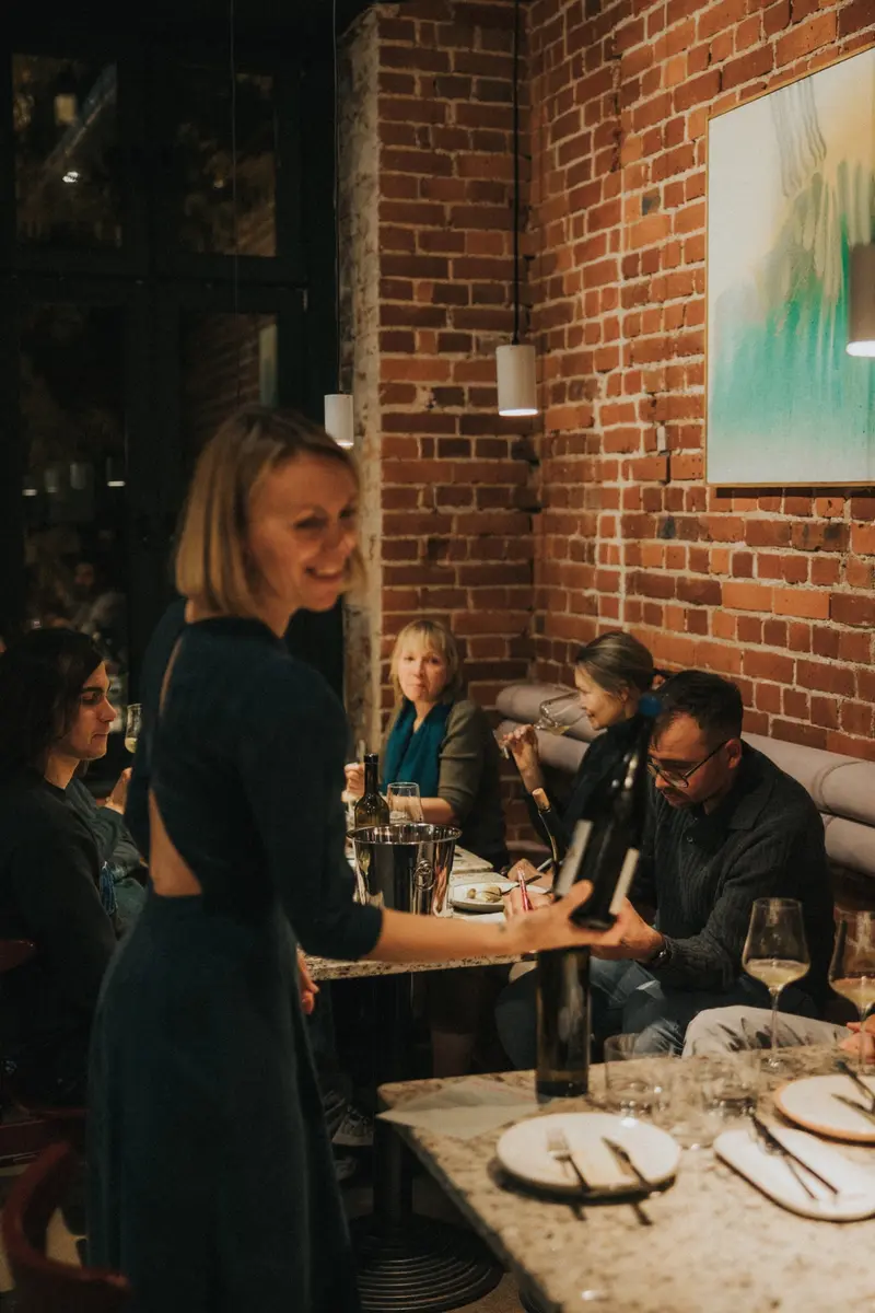 Dominika prezentuje butelkę wina gościom podczas degustacji w Pijalnych